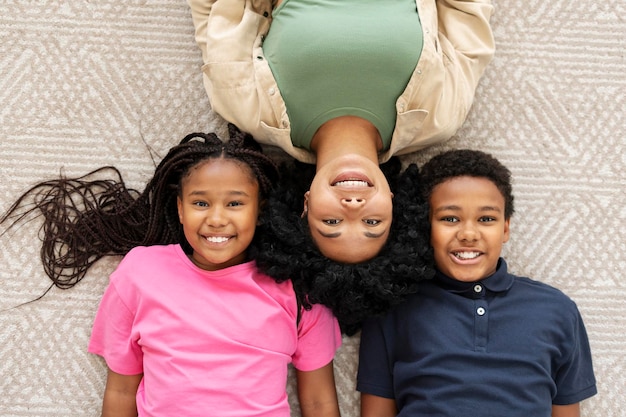 Photo femme afro-américaine et ses enfants, fille et fils, allongés sur le sol, souriant, regardant la caméra