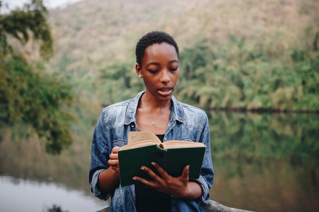 Femme afro-américaine seule dans la nature, lisant un concept de loisirs livre