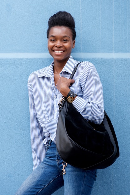 Femme afro-américaine souriant avec sac à main contre le mur bleu