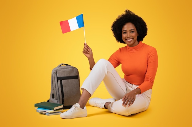 Une femme afro-américaine souriante aux cheveux bouclés assise les jambes croisées sur le sol.