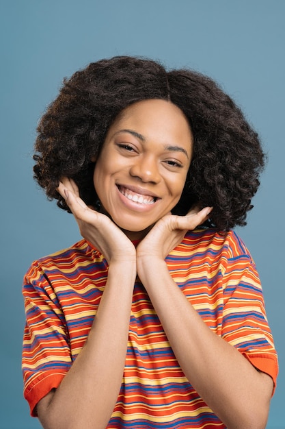 Photo femme afro-américaine souriante aux cheveux bouclés touchant son visage en regardant la caméra