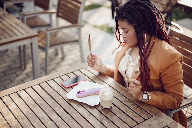 Femme afro-américaine souriante buvant du café et mangeant un dessert dans un café en plein air