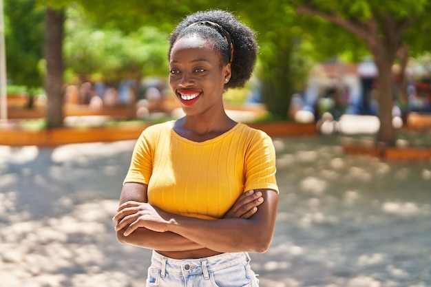 Femme afro-américaine souriante confiante debout avec les bras croisés geste au parc