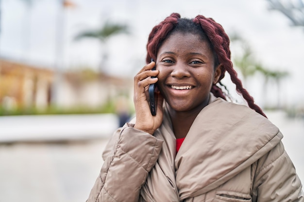 Femme afro-américaine souriante confiante parlant sur le smartphone au parc