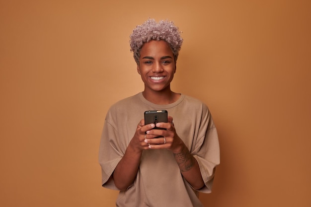 Une femme afro-américaine souriante avec une coupe de cheveux bouclée blonde tape un message texte sur un téléphone portable...