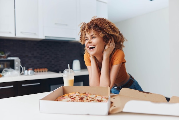 Une femme afro-américaine souriante dégustant une délicieuse pizza dans le confort de sa cuisine.