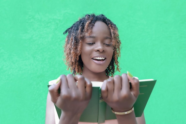 Une femme afro-américaine souriante lit un livre sur fond vert Education Retour à l'école