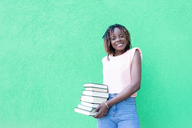 Une femme afro-américaine souriante avec des livres dans ses mains sur un fond vert Émotions positives