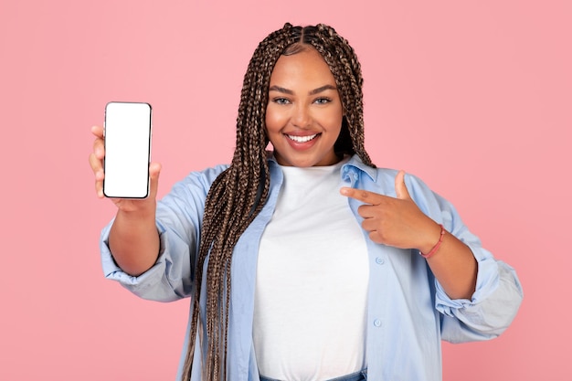 Une femme afro-américaine souriante montrant un écran de téléphone portable tourné en studio