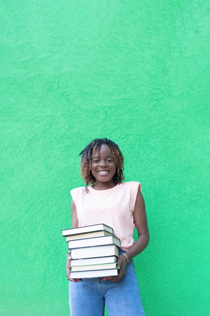 Une femme afro-américaine souriante tient une pile de livres sur un fond vert Espace de copie