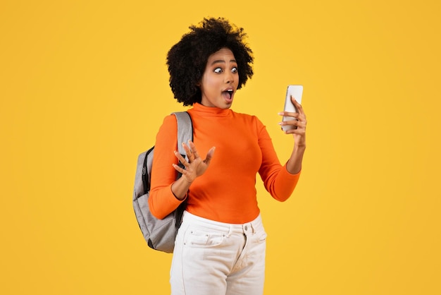 Une femme afro-américaine surprise aux cheveux bouclés portant un col roulant orange et un sac à dos gris