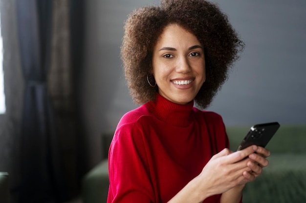 Femme afro-américaine en tenue décontractée rouge utilisant un téléphone portable travaillant la messagerie texte en ligne