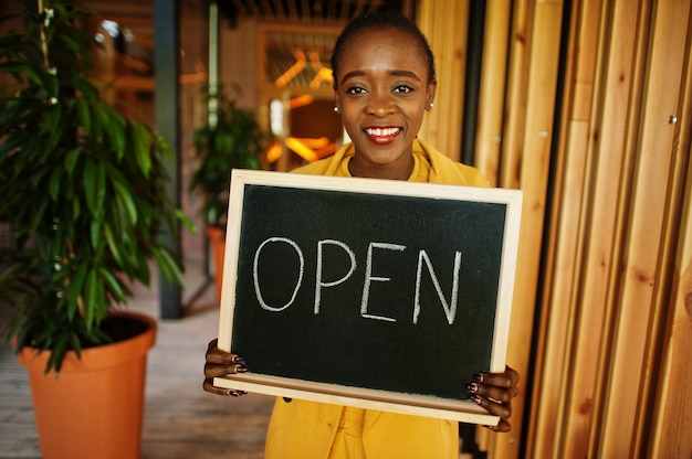 Photo une femme afro-américaine tient un panneau de bienvenue ouvert dans un café-café moderne prêt à servir, un restaurant, un magasin de détail, un propriétaire de petite entreprise.