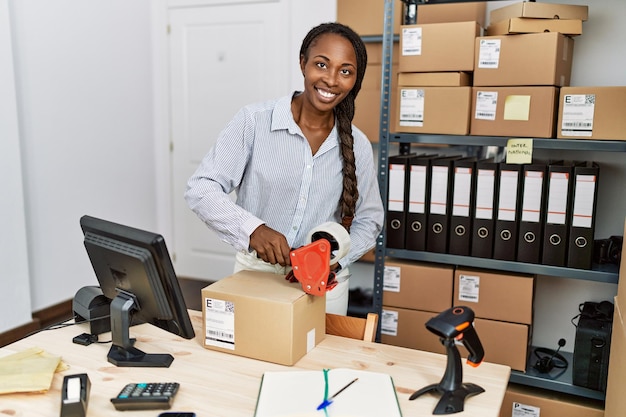 Une femme afro-américaine travaillant dans une entreprise de commerce électronique emballant une boîte en carton au bureau