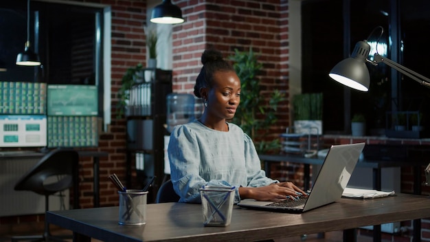 Femme afro-américaine travaillant sur un ordinateur portable pour créer des ventes d'actions, acheter et vendre de l'argent sur le marché des changes. Stratégie d'investissement financier avec statistiques et chiffres commerciaux.