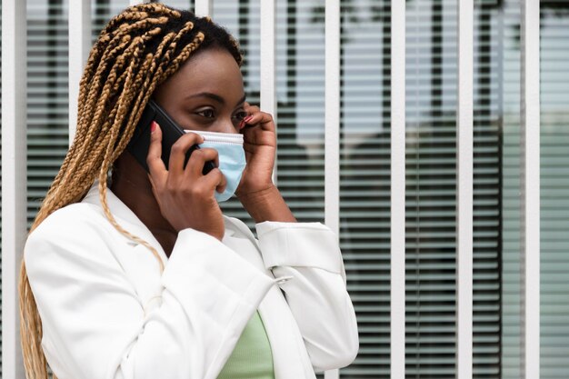 Femme afro-américaine avec des tresses parlant avec un téléphone portable portant un masque protecteur Copy space