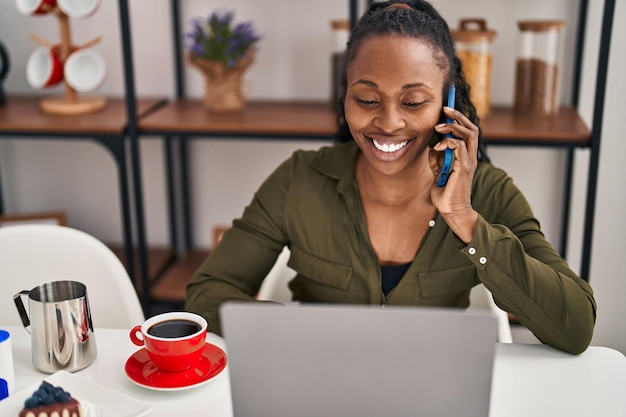 Femme afro-américaine utilisant un ordinateur portable parlant sur le smartphone à la maison