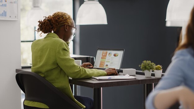 Femme afro-américaine vérifiant le rapport annuel sur pc, regardant les résultats de l'entreprise et la recherche de croissance. Chef d'entreprise analysant les statistiques pour augmenter les bénéfices de l'entreprise sur le lieu de travail.