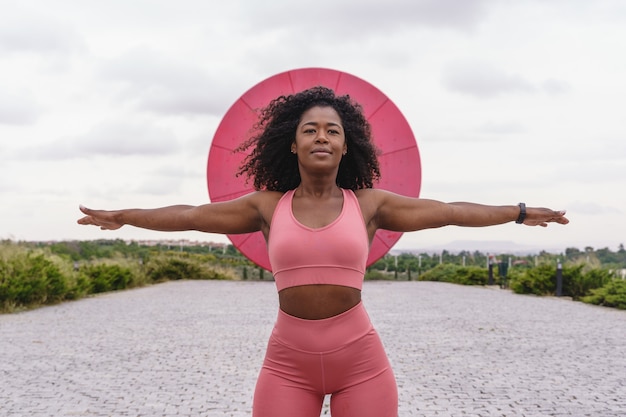 Femme afro-américaine en vêtements de sport roses. Vue horizontale de la femme de remise en forme qui s'étend à l'extérieur