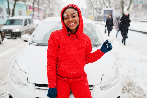 Femme afro-américaine en voiture propre à capuche rouge de la neige en journée d'hiver.