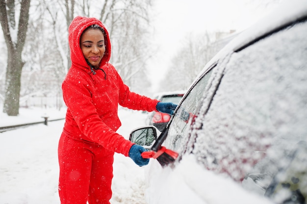 Femme afro-américaine en voiture propre à capuche rouge de la neige en journée d'hiver.