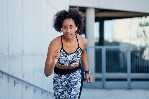 Femme afro athlétique en cours d'exécution et faire de l'exercice à l'extérieur