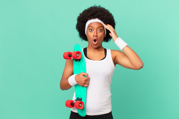 Femme afro ayant l'air heureuse, étonnée et surprise, souriante et réalisant une bonne nouvelle incroyable et incroyable. concept de planche à roulettes