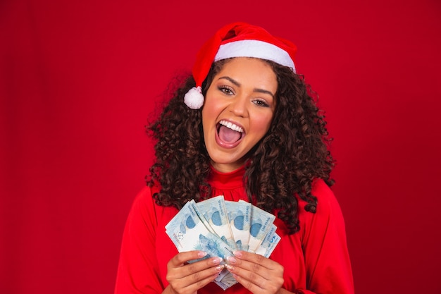 Femme afro comptant les billets d'argent brésiliens. De vraies notes. 100 billets de reais. Concept d'épargne pour la fin de l'année. Passez Noël. Dépensé en cadeaux de Noël.