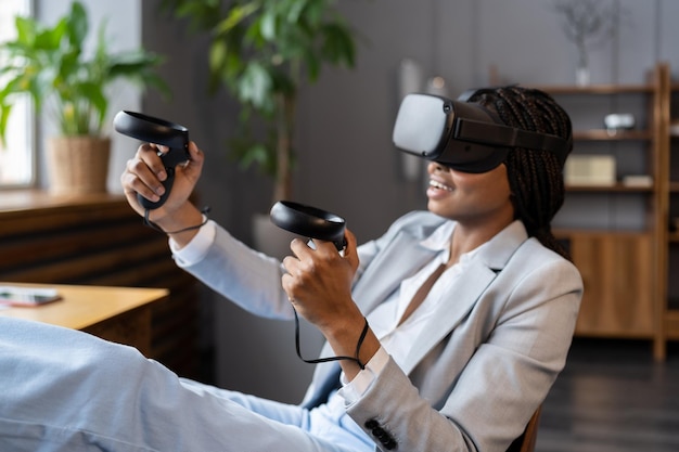 Une femme afro excitée porte des lunettes vr et tient l'expérience du joystick du casque de réalité virtuelle pour les entreprises