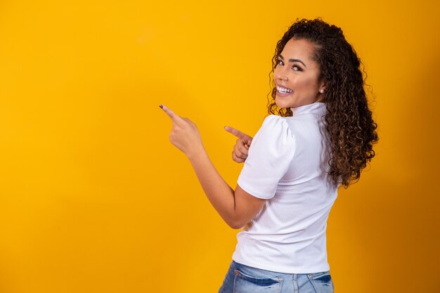 Une femme afro gaie pointe vers l'espace de copie, discute d'une promo incroyable, donne un lieu ou une direction. Femme avec son dos pointant sur le côté