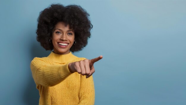Une femme afro joyeuse pointe sur l'espace de copie donne le chemin ou la direction porte un pull jaune chaud h