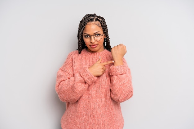 Une femme afro noire qui a l'air impatiente et en colère pointant vers la montre demandant la ponctualité veut être à l'heure