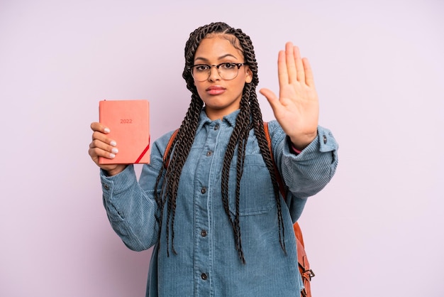 Femme afro noire à la recherche sérieuse montrant la paume ouverte faisant un geste d'arrêt calendrier étudiant ou concept d'agenda