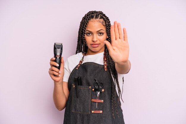 Photo femme afro noire à la recherche sérieuse montrant la paume ouverte faisant un geste d'arrêt. concept de salon de coiffure