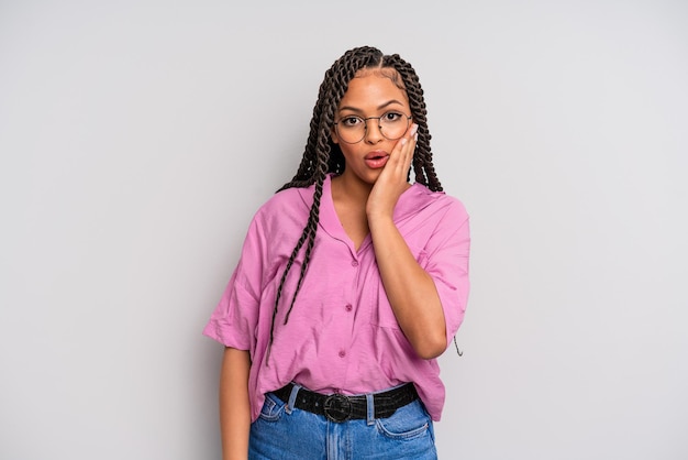 Femme afro noire se sentant choquée et étonnée tenant face à main dans l'incrédulité avec la bouche grande ouverte