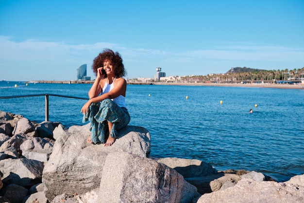 Une femme afro noire sinueuse utilisant un smartphone sur la plage de Barcelone