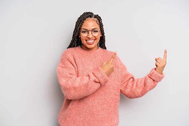 Femme afro noire souriant joyeusement et pointant vers le côté et vers le haut avec les deux mains montrant l'objet dans l'espace de copie