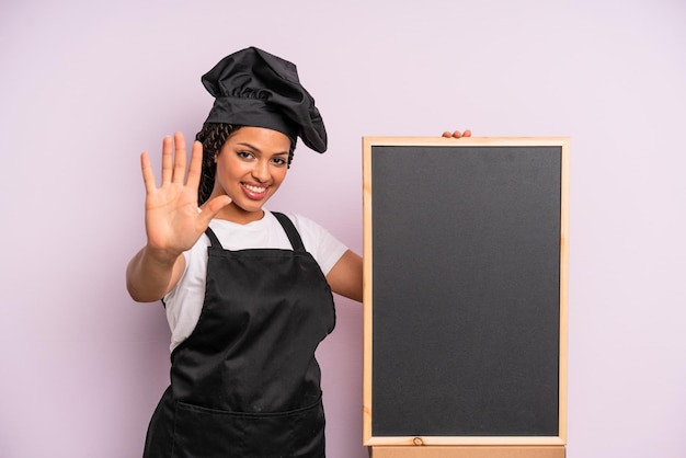 Femme afro noire souriante et amicale montrant le concept du chef numéro cinq et du tableau noir