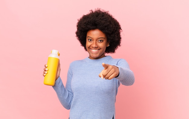 Femme afro pointant vers la caméra avec un sourire satisfait, confiant et amical, vous choisissant. concept de smoothie