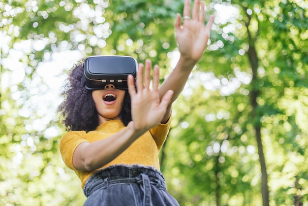 Femme afro portant des lunettes de réalité virtuelle dans un jardin. Mise au point sélective.