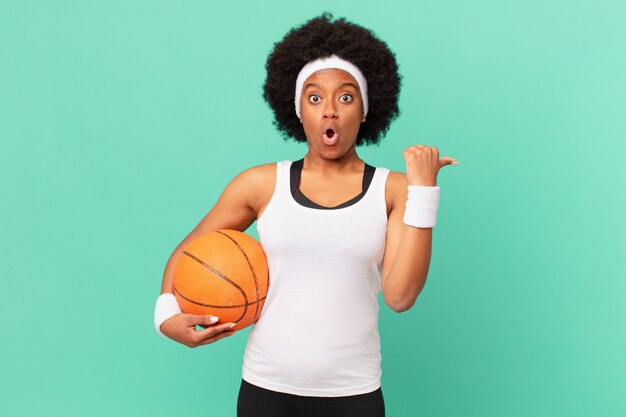 Femme afro semblant étonnée d'incrédulité, pointant l'objet sur le côté et disant wow, incroyable. concept de basket-ball