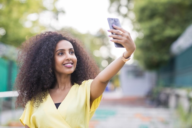 Une femme afro souriante aux cheveux bouclés prenant un selfie au coucher du soleil comprend un espace de copie et de texte