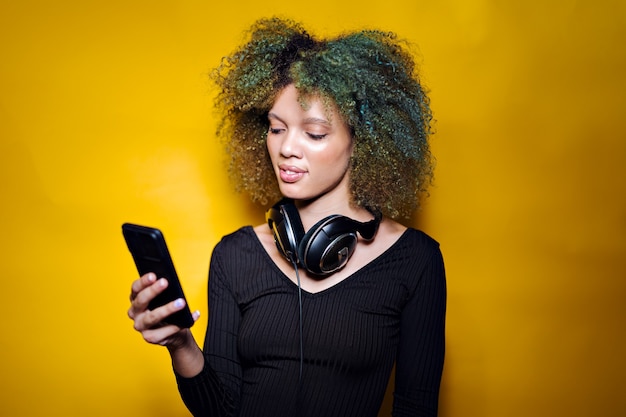 Femme afro avec téléphone portable et casque sur fond jaune