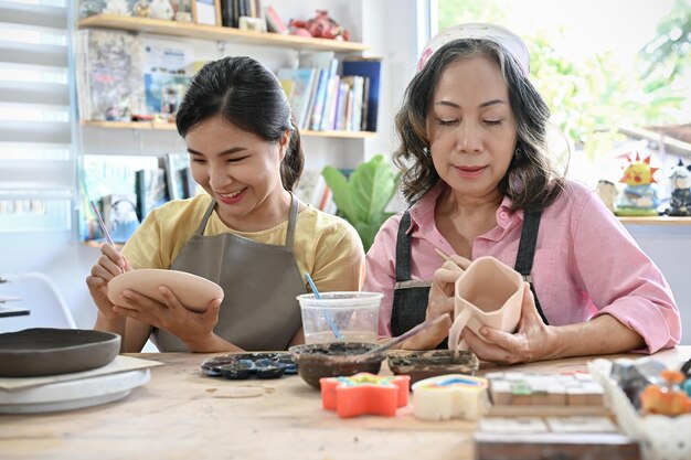 Une femme d'âge asiatique détendue et une jeune femme se sont concentrées à peindre leur tasse en céramique faite à la main