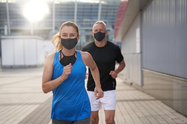 Femme d'âge moyen active portant un masque de protection tout en courant avec son mari à l'extérieur