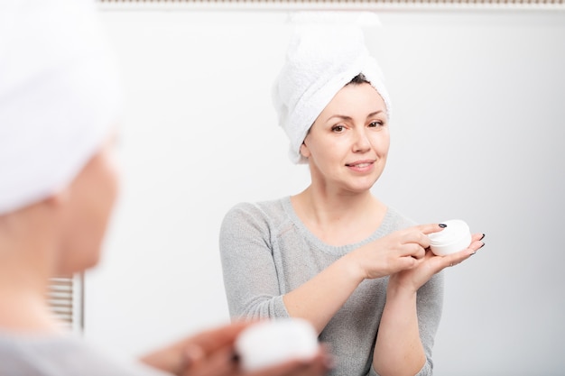 Femme d'âge moyen appliquant une crème anti-âge avant miroir à la maison