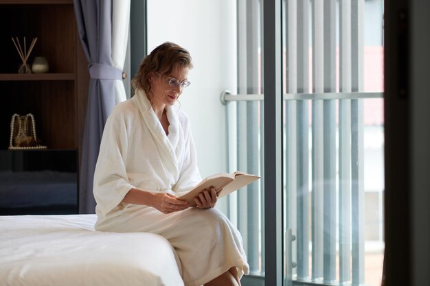 Femme d'âge moyen appréciant la lecture d'un bon livre dans la chambre d'hôtel