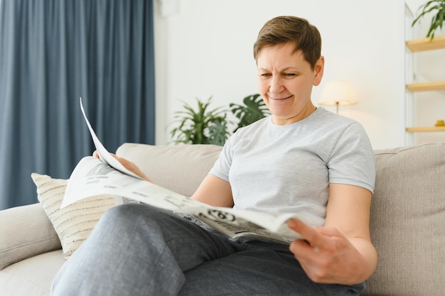 Femme d'âge moyen assise sur un canapé et lisant des journaux