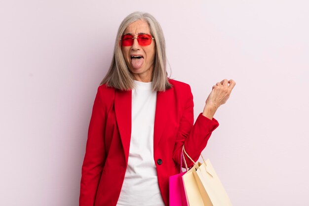 Femme d'âge moyen avec une attitude joyeuse et rebelle plaisantant et tirant la langue du concept de magasinage