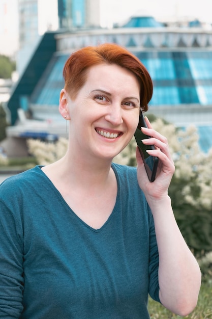 Femme d'âge moyen aux cheveux rouges dans un quartier d'affaires moderne et parlant au téléphone Une femme utilise un smartphone en se promenant dans la ville Une femme souriante et regardant la caméra
